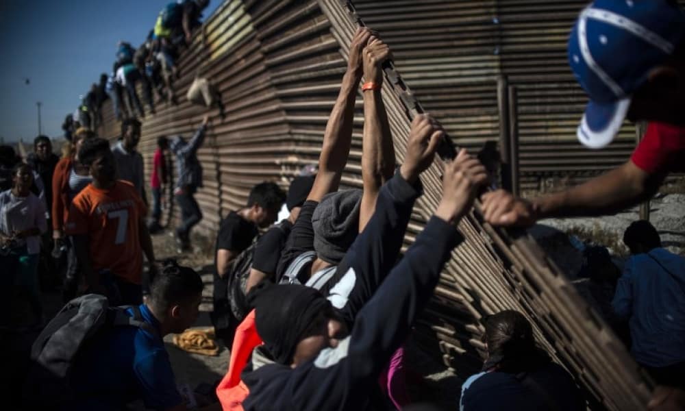 Migrantes saltan la barrera que divide México con EU en Tijuana.